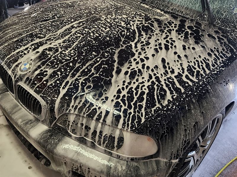 Black BMW M5 covered in snow foam during a pre-wash